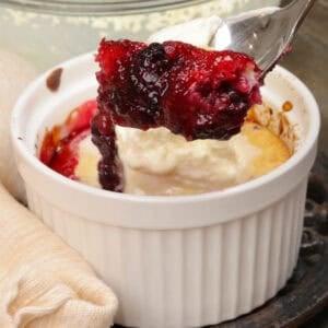 a blackberry cobbler topped with whipped cream and a spoon on the side of the dish.