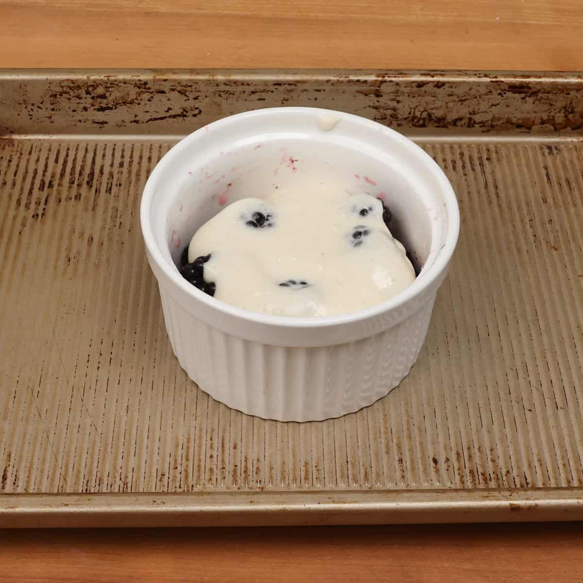 an unbaked blackberry cobbler in a ramekin on a baking sheet.