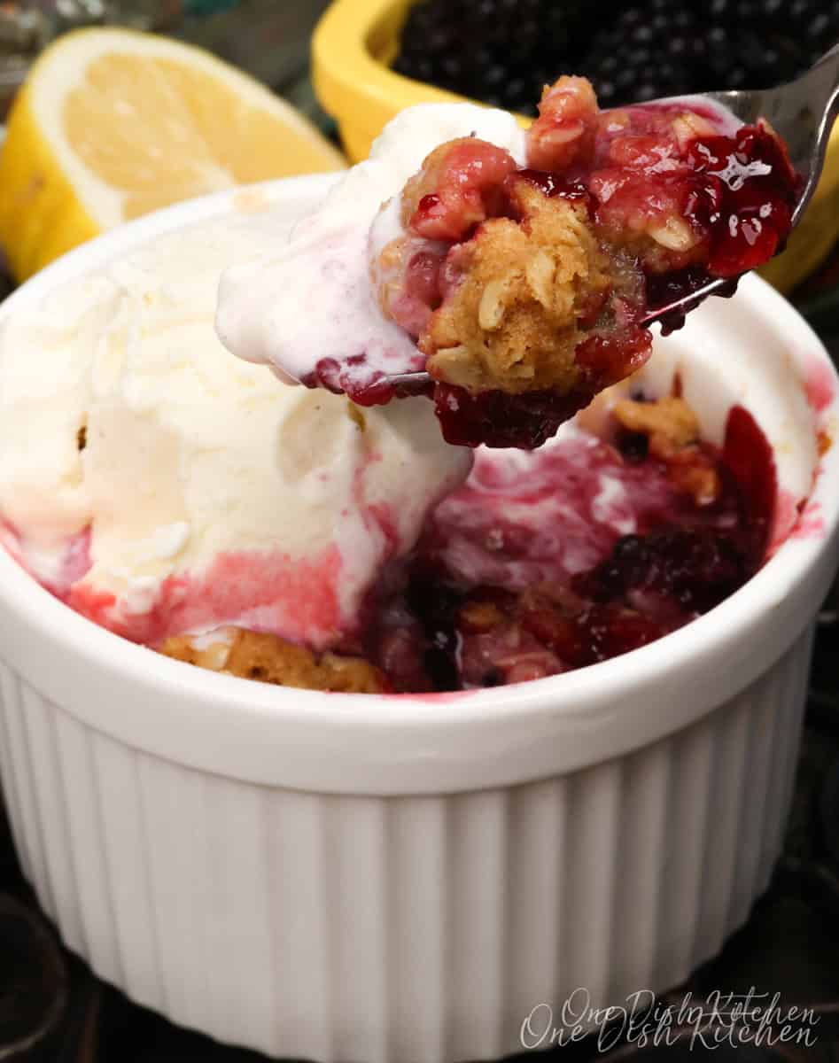 an individual blackberry crisp in a white ramekin topped with vanilla ice cream.