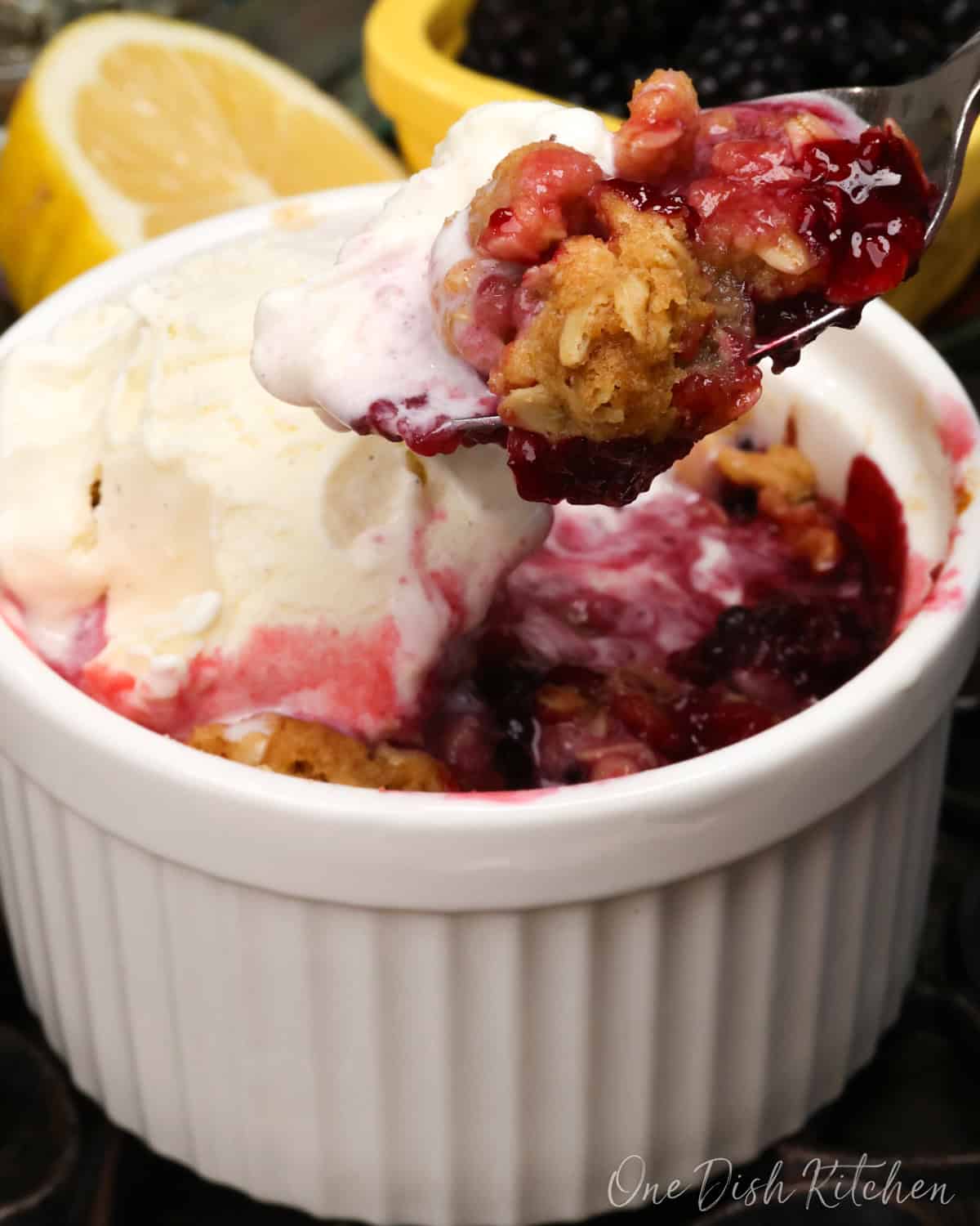 an individual blackberry crisp in a white ramekin topped with vanilla ice cream.