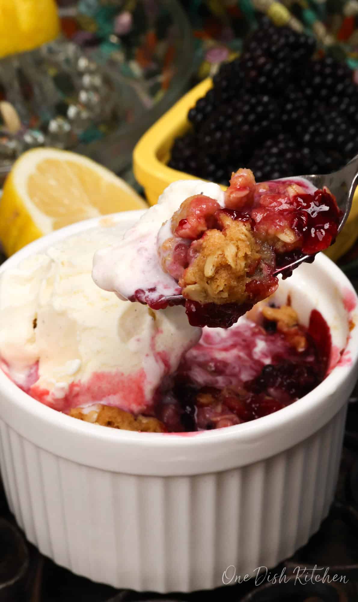 a blackberry crisp with vanilla ice cream and a spoon on the side scooping it up.