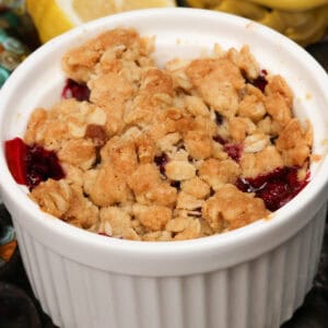 a blackberry crisp in a small ramekin next to a bowl of blackberries and fresh lemons.