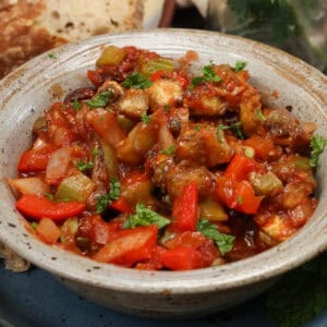 a bowl of caponata next to fresh parsley and slices of bread.