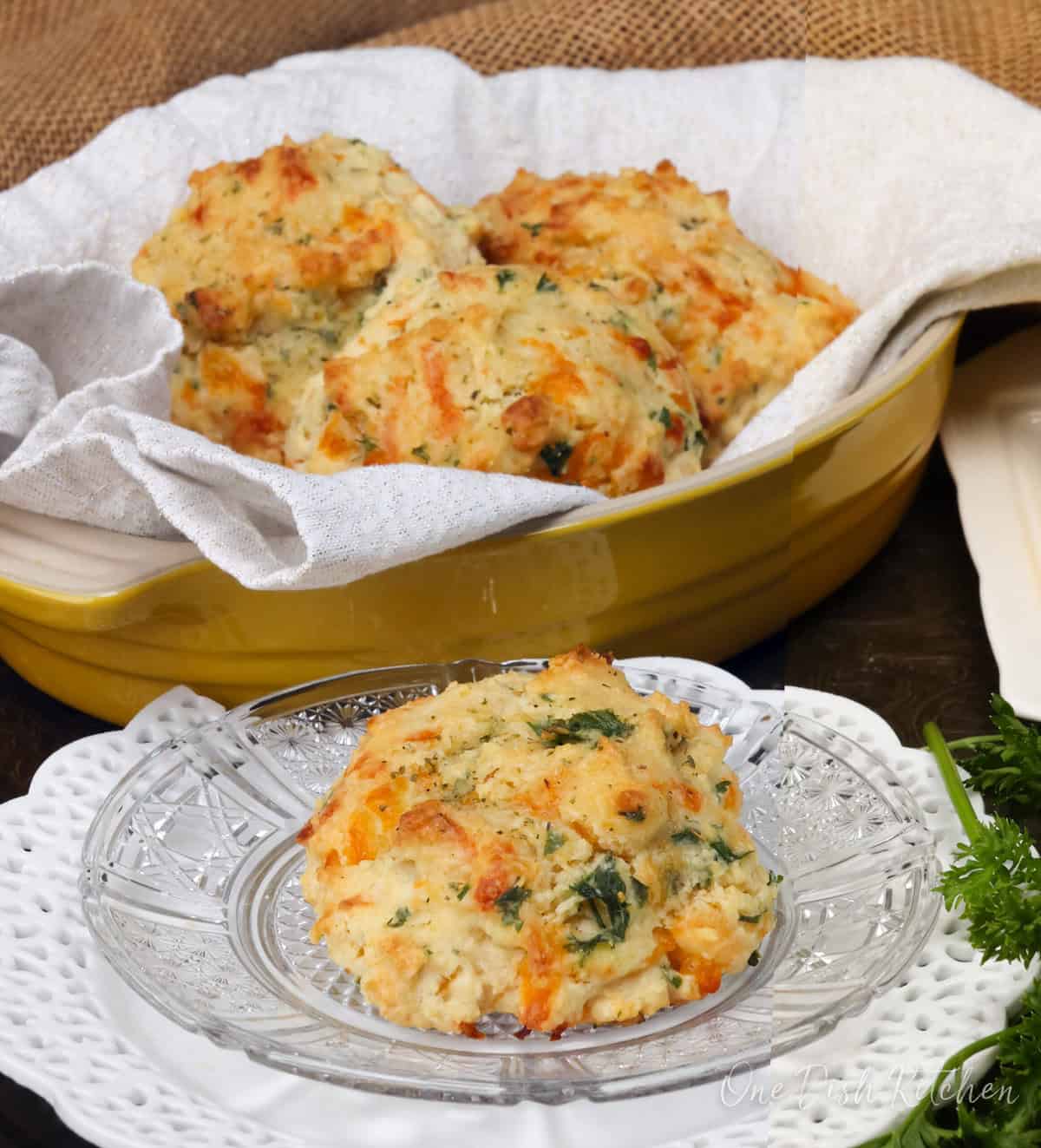 one cheddar biscuit on a plate next to a basket of biscuits.