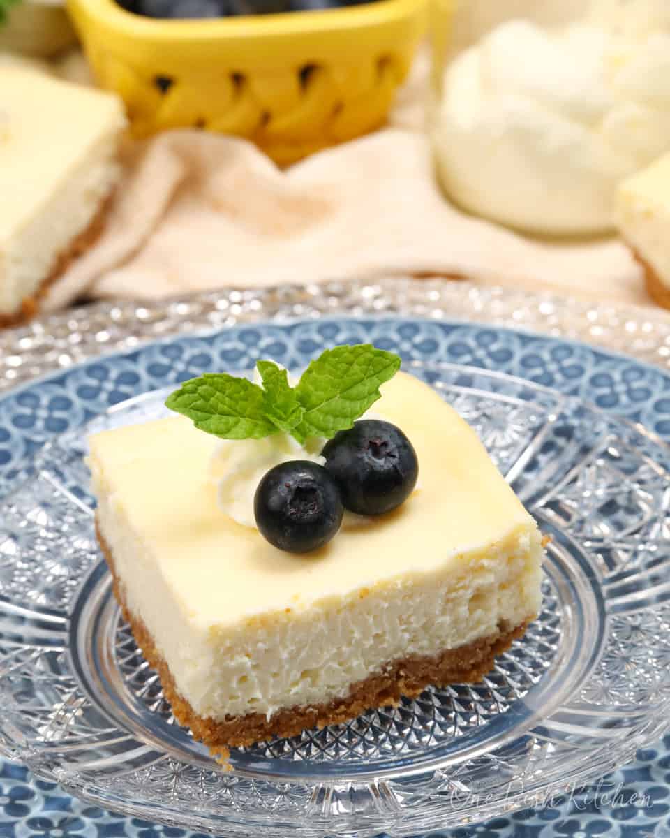a cheesecake square topped with blueberries and fresh mint next to three other cheesecake bars.