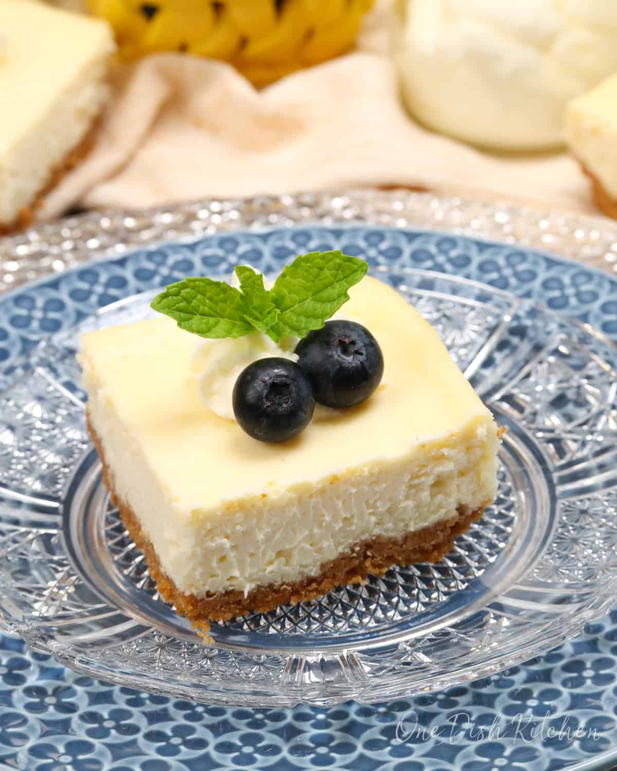 one cheesecake bar on a blue plate topped with fresh mint and blueberries.