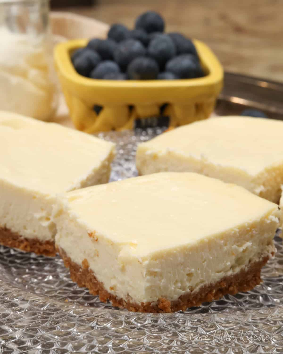 four cheesecake bars on a clear plate.