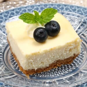 a cheesecake square topped with blueberries and fresh mint next to three other cheesecake bars.