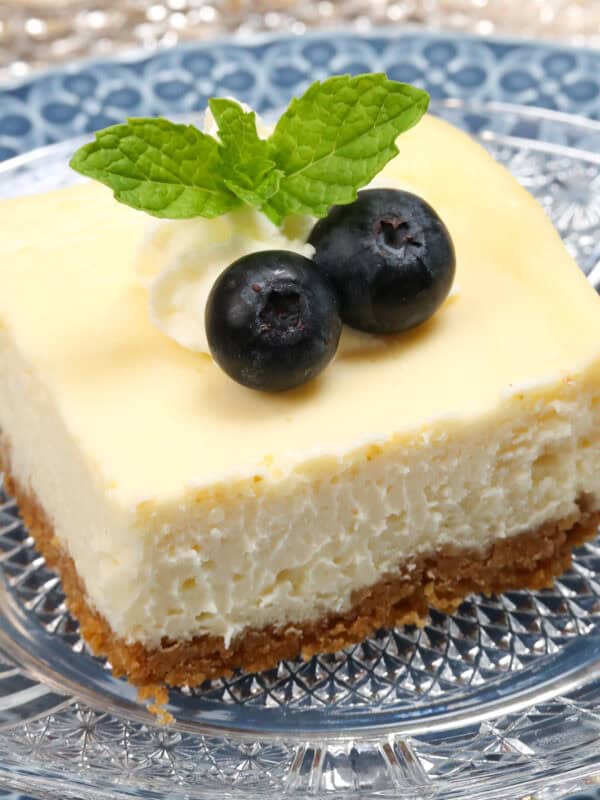 a cheesecake square topped with blueberries and fresh mint next to three other cheesecake bars.