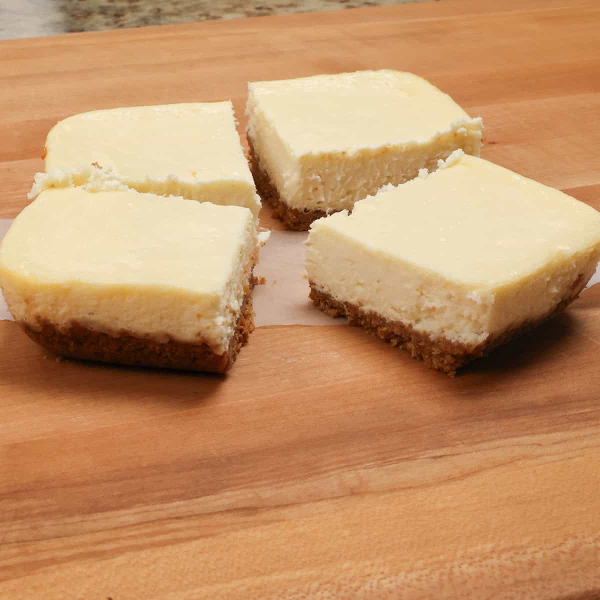 four cheesecake bars on a cutting board.