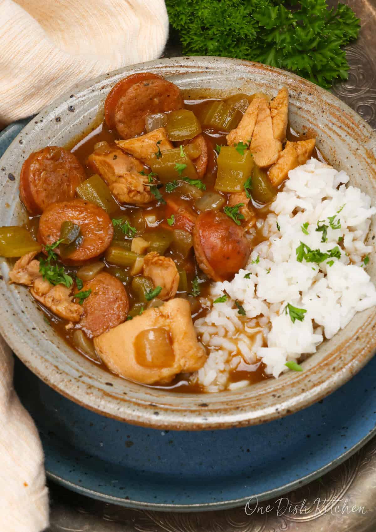 a bowl of gumbo with chicken and sausage next to white rice.