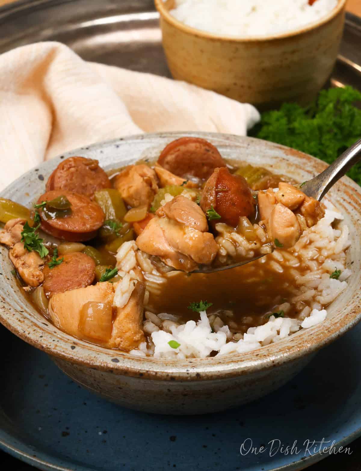 chicken and sausage gumbo in a brown bowl with a spoon on the side.