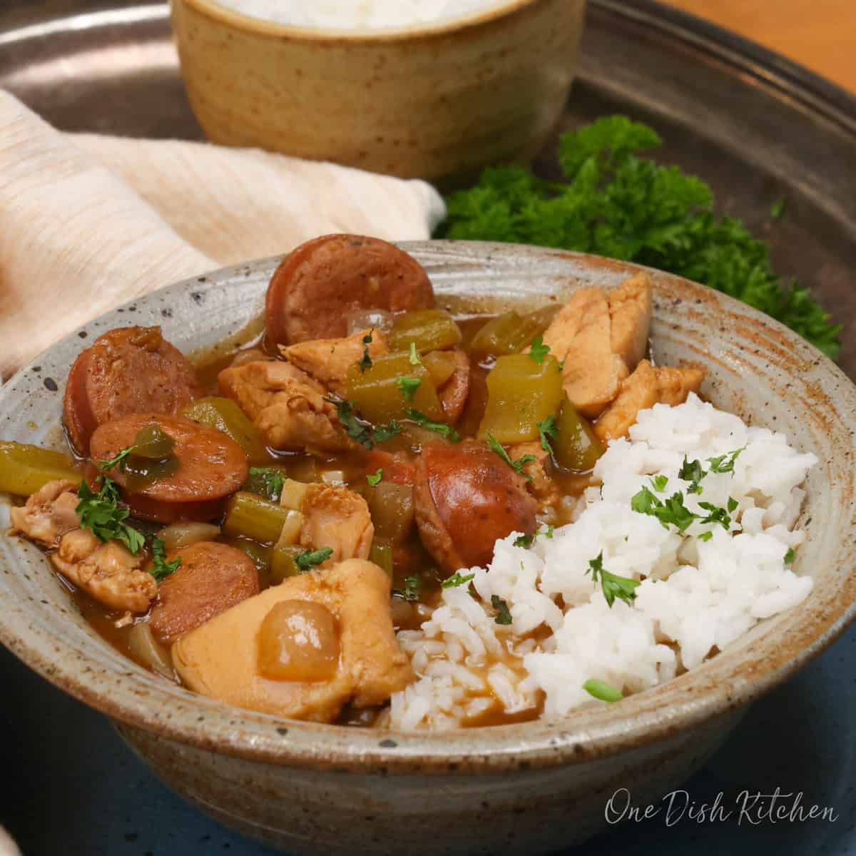 a brown bowl filled with chicken and sausage gumbo and rice on a silver tray.