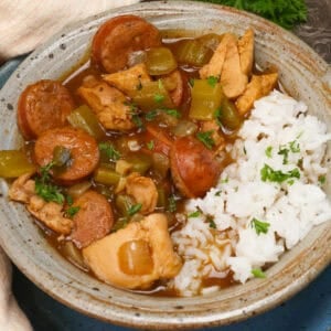 a bowl of gumbo with chicken and sausage next to white rice.