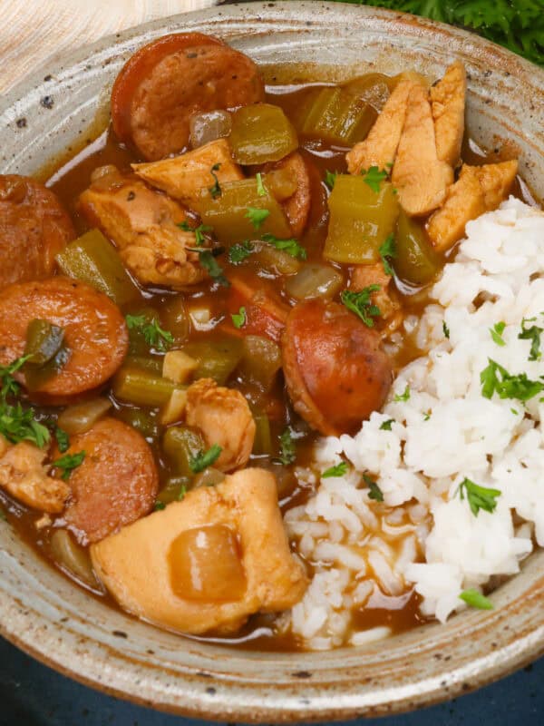 a bowl of gumbo with chicken and sausage next to white rice.