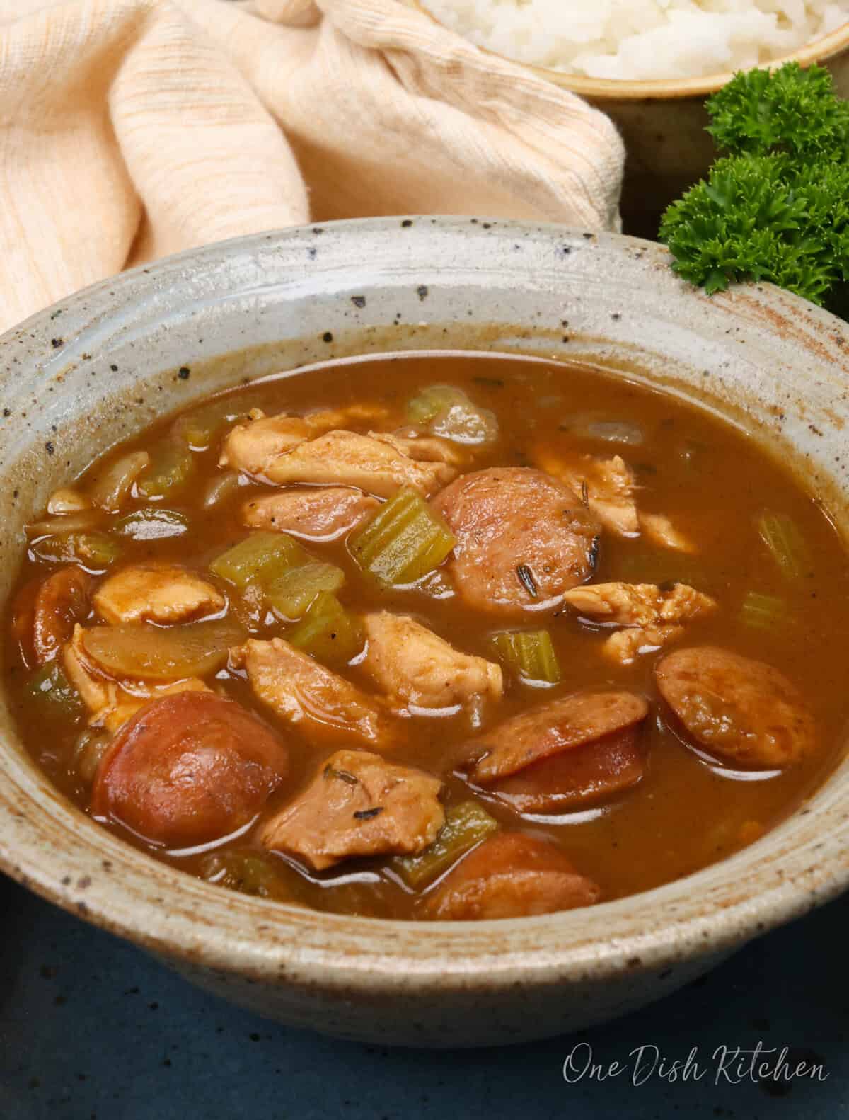 a bowl of chicken and sausage gumbo next to a brown napkin.