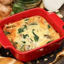 a crustless quiche with spinach and mushrooms in a red square baking dish.