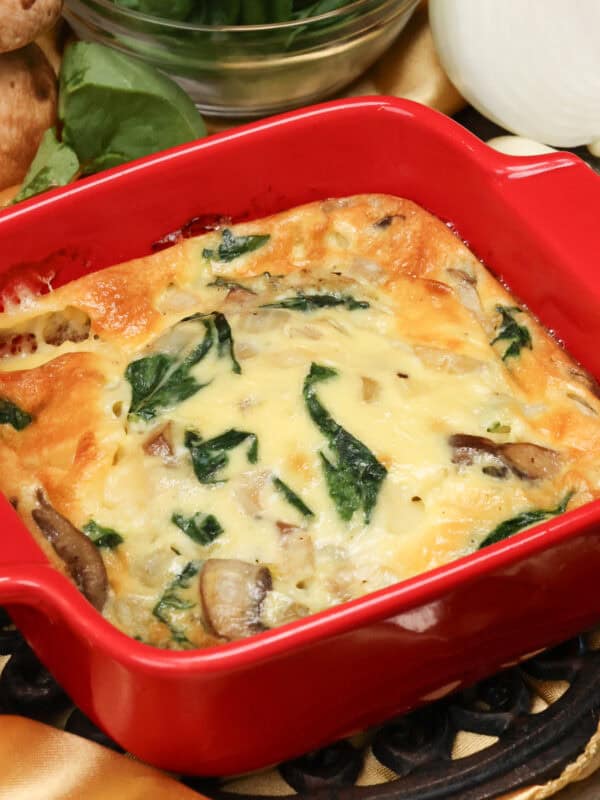 a crustless quiche with spinach and mushrooms in a red square baking dish.