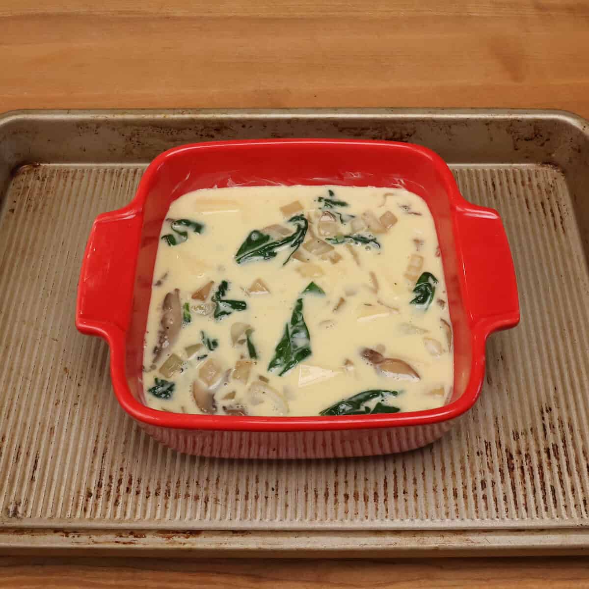 a small unbaked spinach mushroom quiche in a baking dish.