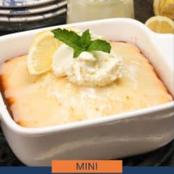 a small lemon cake in a square baking dish next to a jar of whipped cream and three plates.