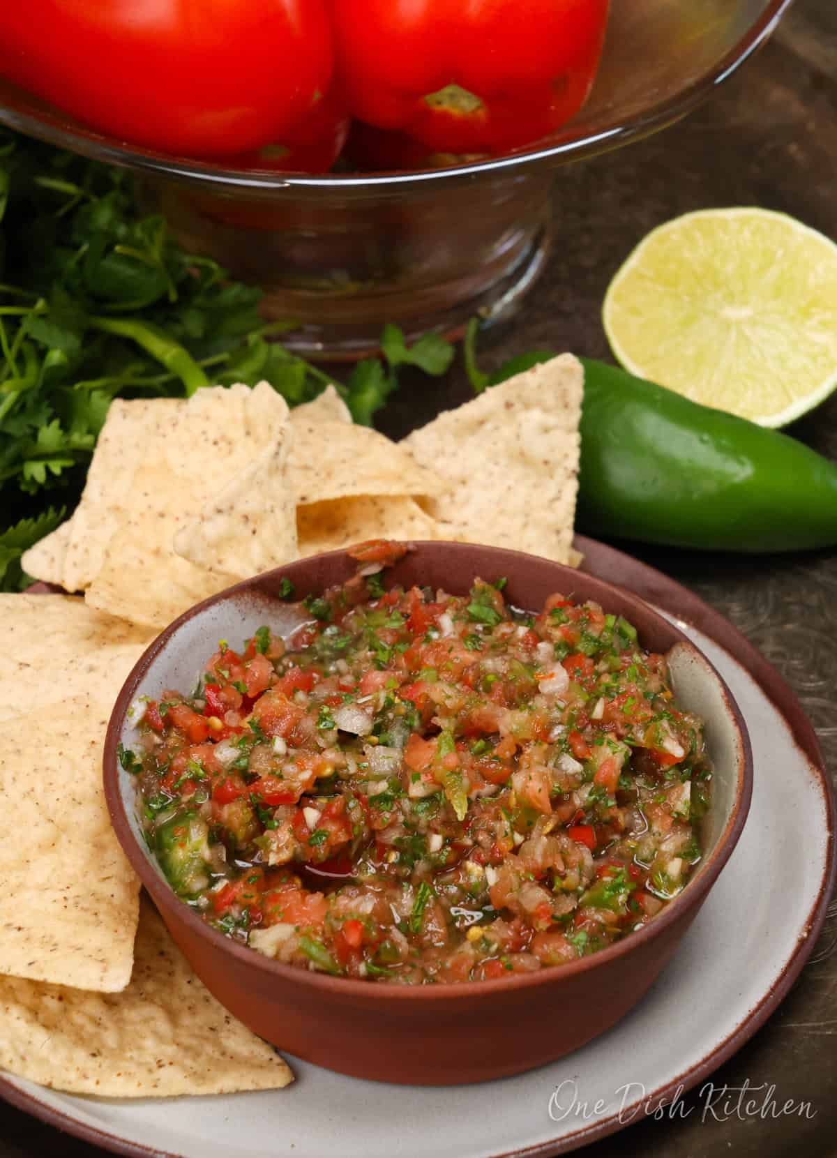 a bowl of fresh salsa next to tortilla chips, a jalapeno and a lime.