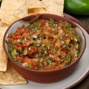 a bowl of fresh salsa next to tortilla chips, a jalapeno and a lime.