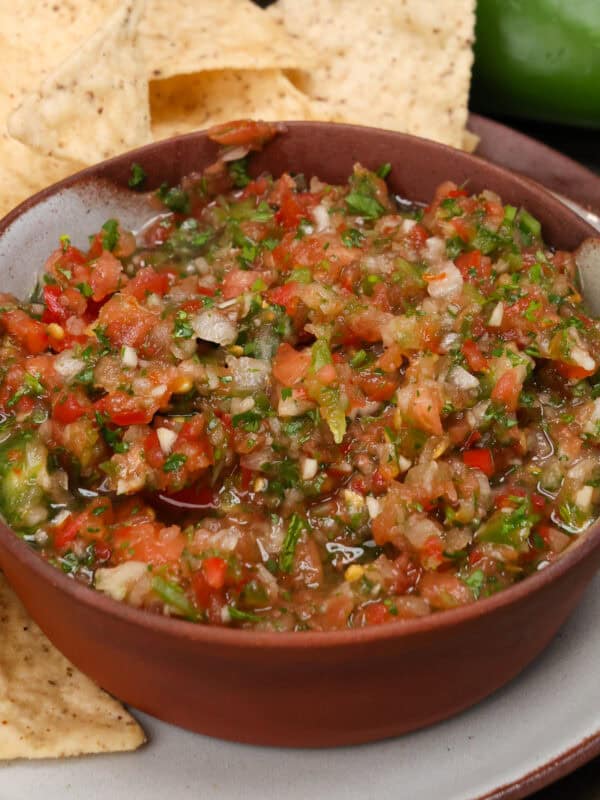 a bowl of fresh salsa next to tortilla chips, a jalapeno and a lime.