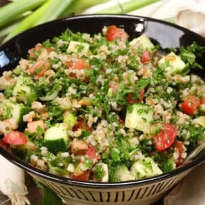 a bowl of tabbouleh on a silver tray next to fresh green onions.