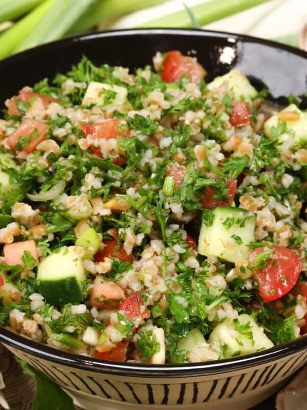 a bowl of tabbouleh on a silver tray next to fresh green onions.