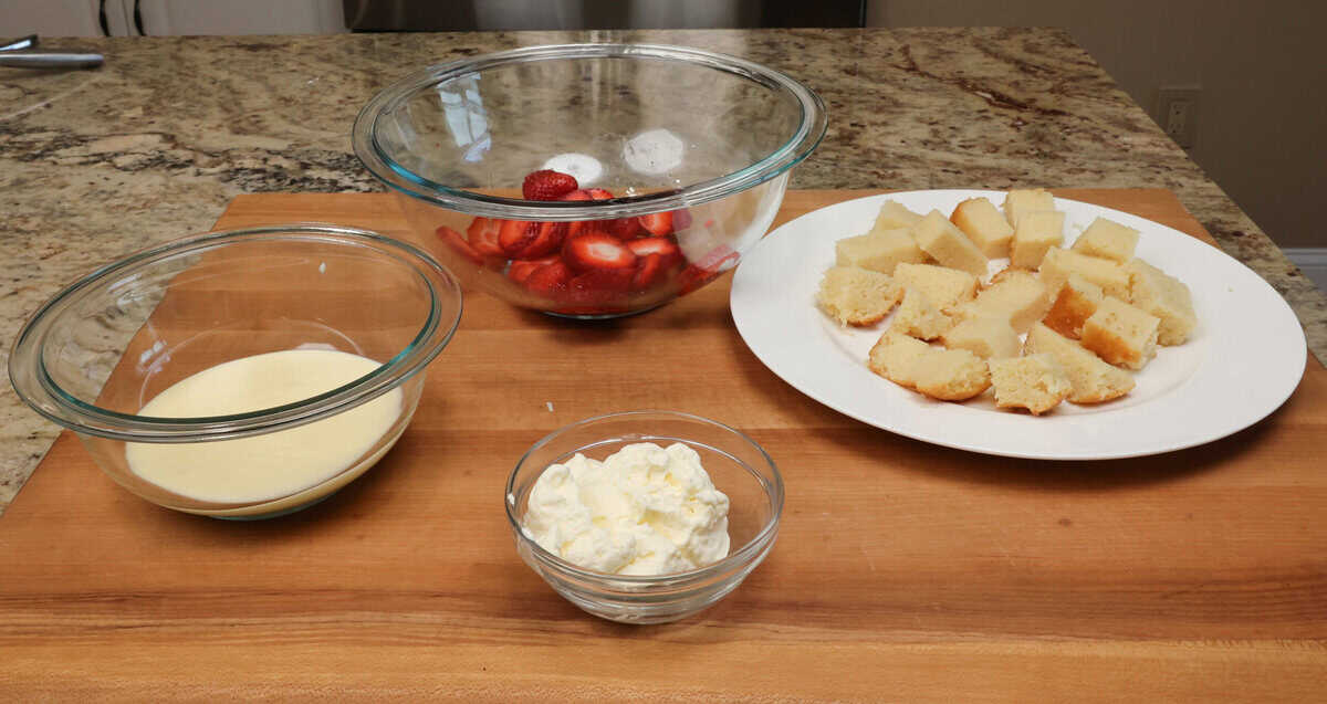 cake, pudding, strawberries, and whipped cream on a kitchen counter.