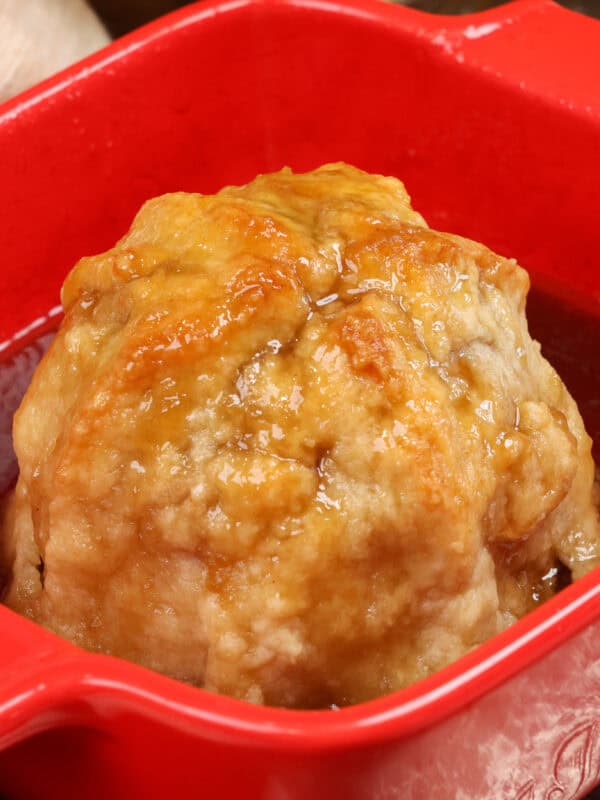 an apple dumpling in a red baking dish with sauce surrounding the apple.