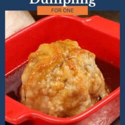 an apple dumpling in a red baking dish with sauce surrounding the apple.