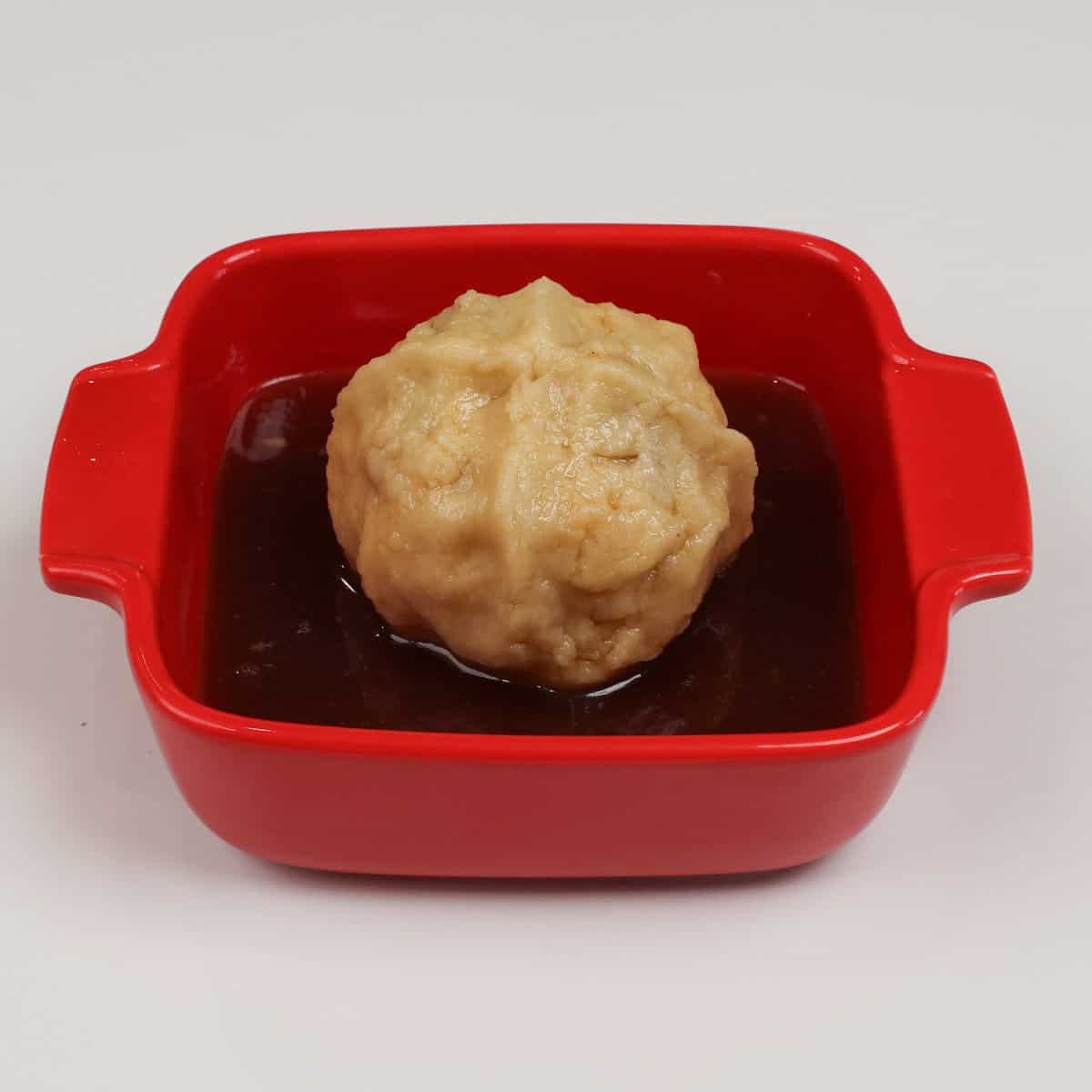 an apple dumpling in a baking dish surrounded by sauce.