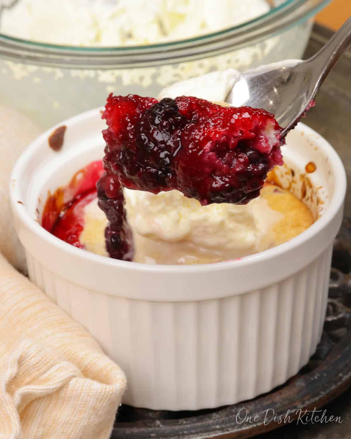 a blackberry cobbler topped with whipped cream and a spoon on the side of the dish.