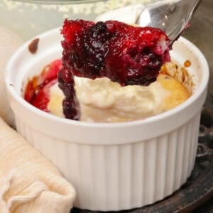 a blackberry cobbler topped with whipped cream and a spoon on the side of the dish.