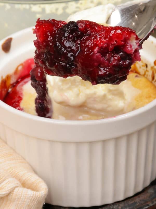 a blackberry cobbler topped with whipped cream and a spoon on the side of the dish.