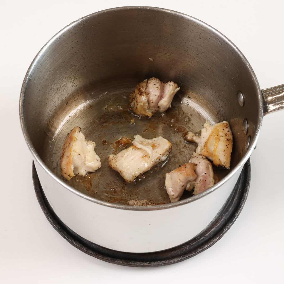 chicken pieces cooking in a small pot.