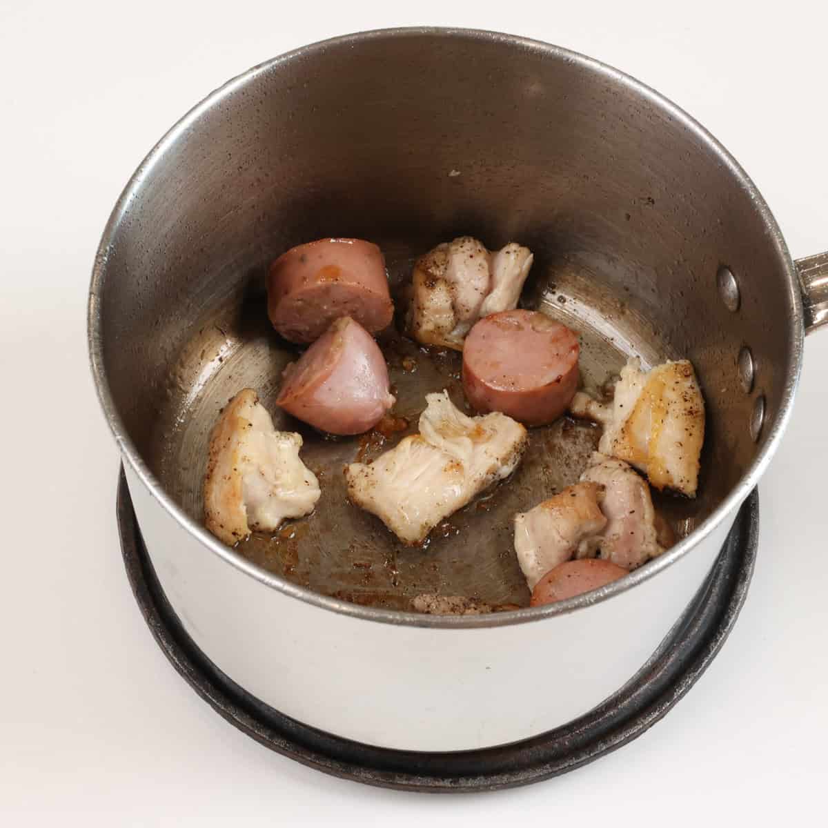 chicken and sausage browning in a saucepan.