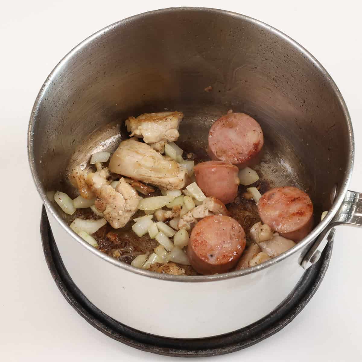 sausage, chicken, onions and garlic cooking in a small pot.