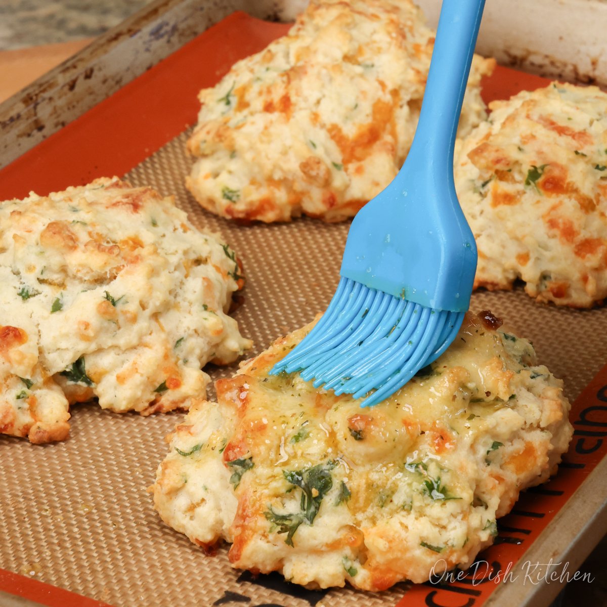 brushing garlic butter over the tops of cheese biscuits on a baking sheet.
