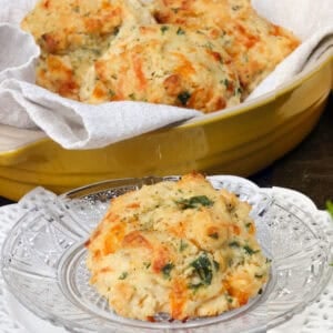 a single cheddar biscuit on a plate next to a basket full of biscuits.