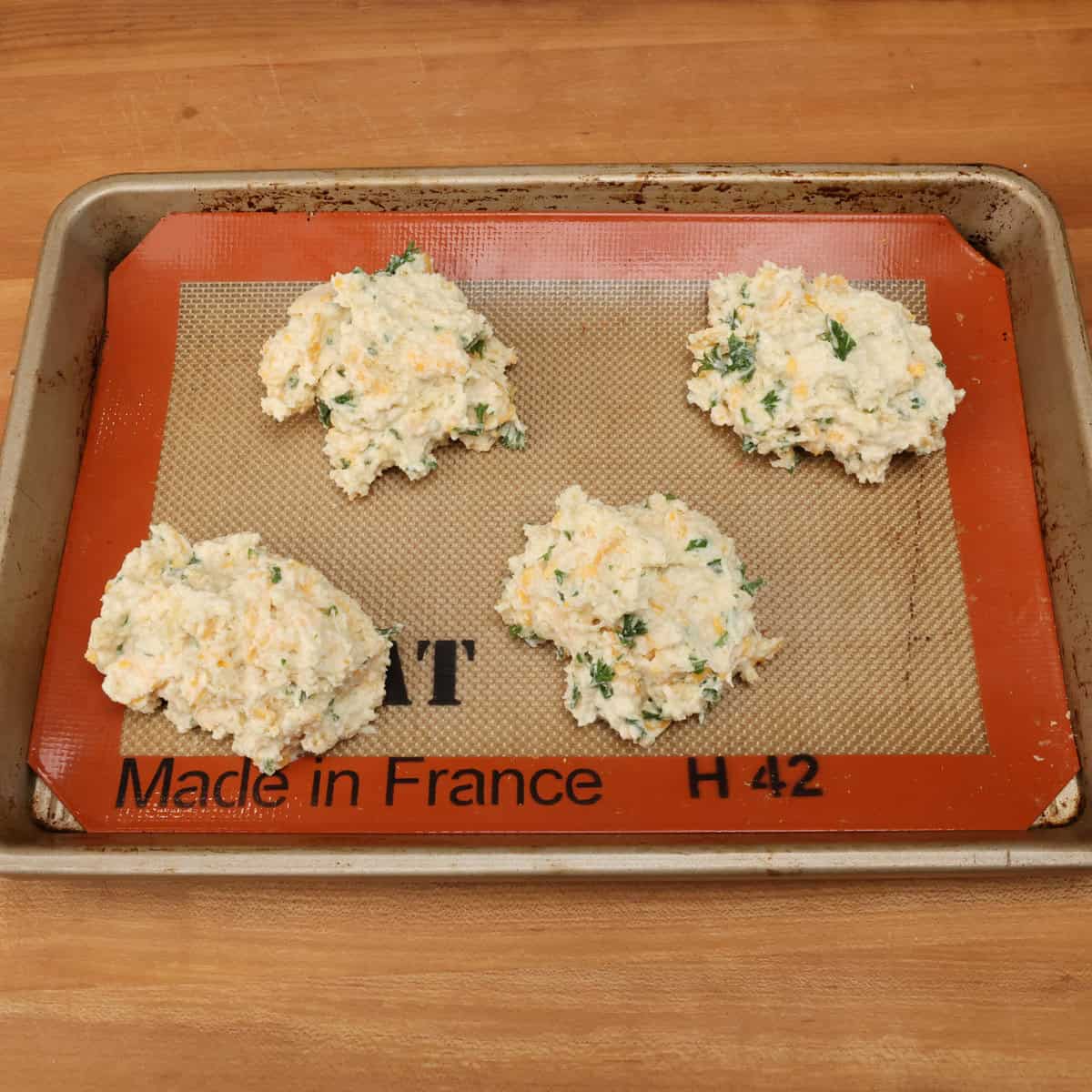 four unbaked cheddar biscuits on a baking sheet.