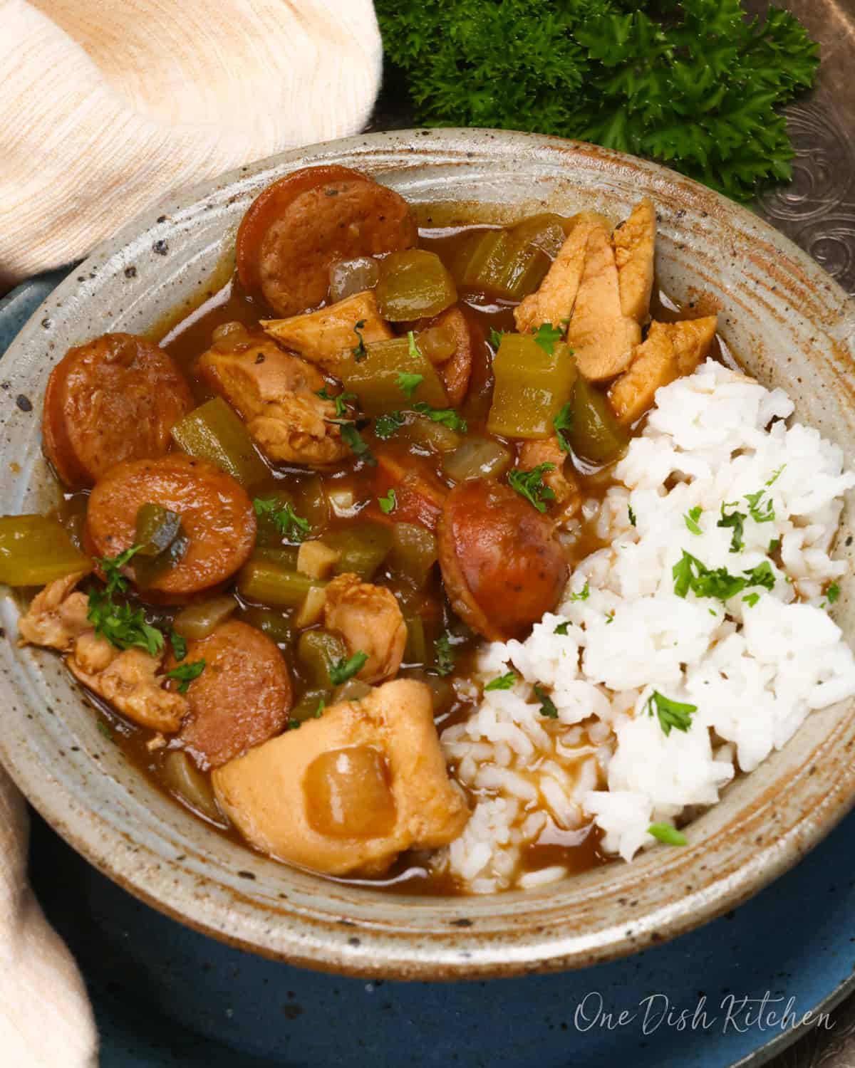a bowl of gumbo with chicken and sausage next to white rice.