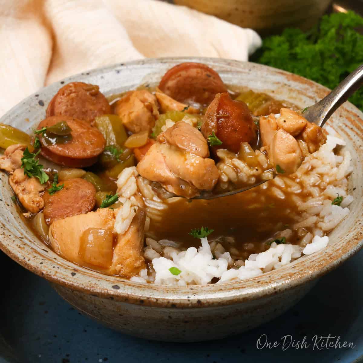 chicken and sausage gumbo in a brown bowl with a spoon on the side.