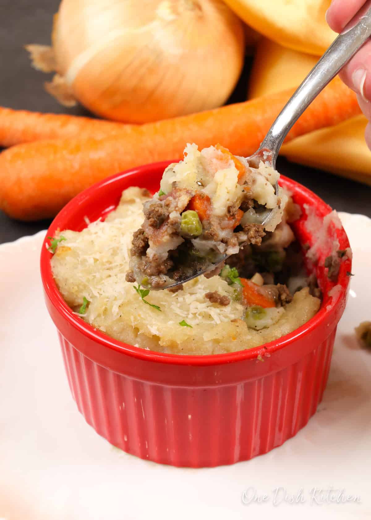 a small cottage pie in a red ramekin with a spoon above the dish.