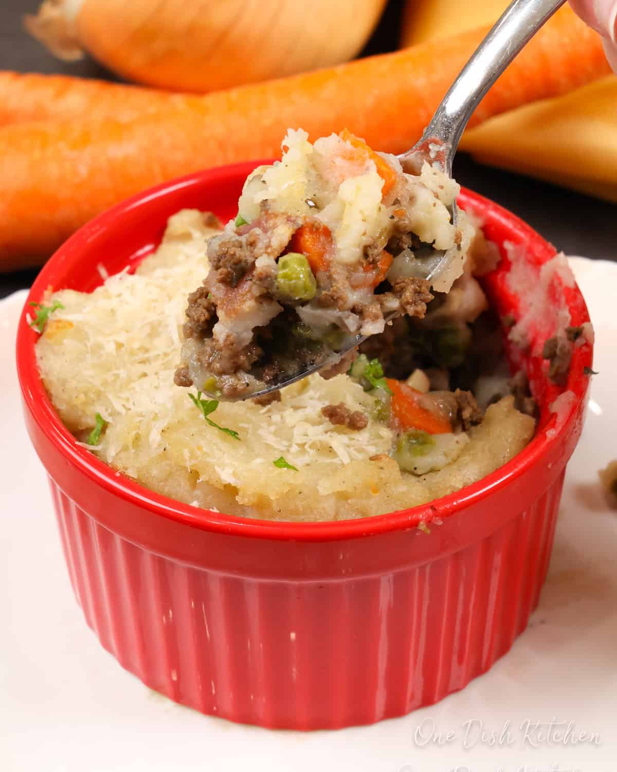 a small cottage pie in a red ramekin with a spoon above the dish.