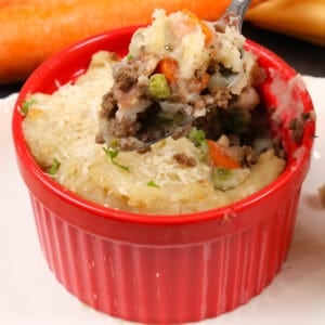 a small cottage pie in a red ramekin with a spoon above the dish.