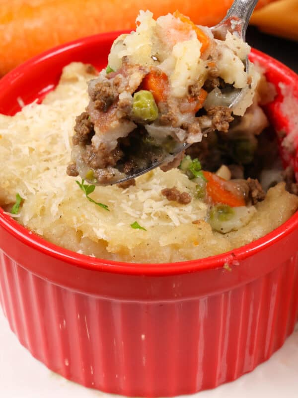 a small cottage pie in a red ramekin with a spoon above the dish.