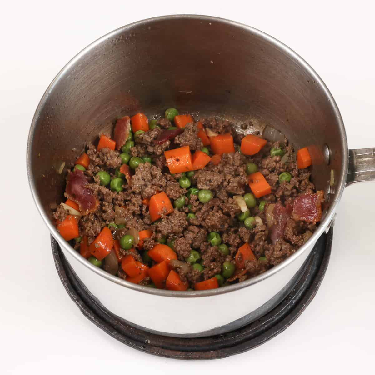 ground beef, vegetables and bacon cooking in a small pot.