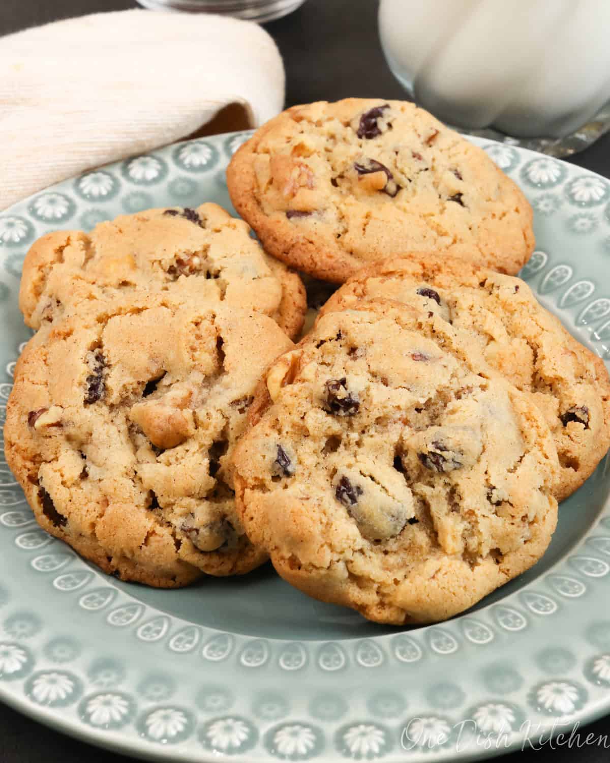 six hermit cookies on a green plate next to a bowl of dates and a glass of milk.